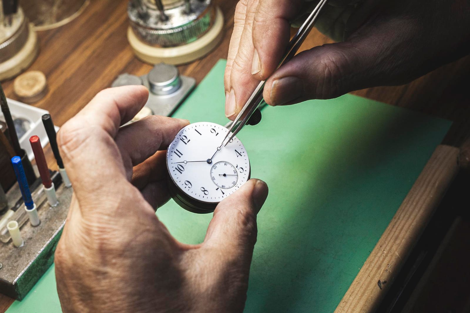 Mani che regolano con la pinzetta le lancette di un quadrante da orologio da tasca